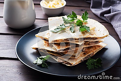Pieces of quesadilla with mushrooms sour cream and cheese on a plate with parsley leaves. Wooden background close up. Stock Photo