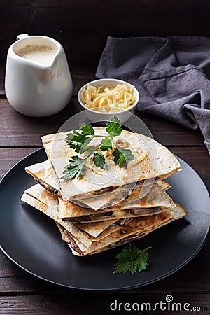 Pieces of quesadilla with mushrooms sour cream and cheese on a plate with parsley leaves. Wooden background copy space. Stock Photo