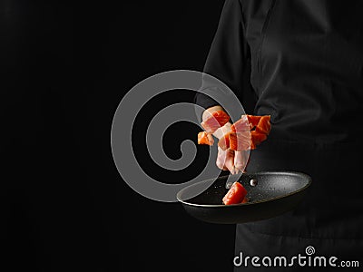 Pieces of red fish in a frying pan. A chef in a black uniform holds a frying pan in his hand, in which, in a state of levitation, Stock Photo