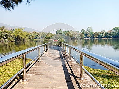 The pier in public park with danger warning sign. Silver handrail with wooden walkway near the lake with landscape view Stock Photo