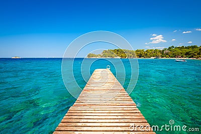 Pier at sea in the summertime. Azure sea and shore with rocks. Clear sea water and clear sky. Stock Photo