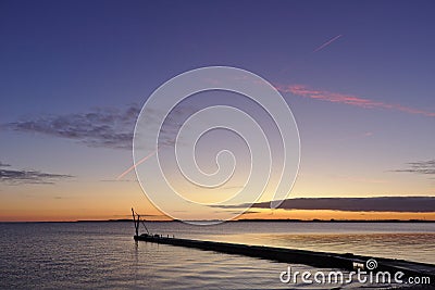 Pier before sunrise with small crane silhouetted against the morning sky and red vapor trail overhead Stock Photo