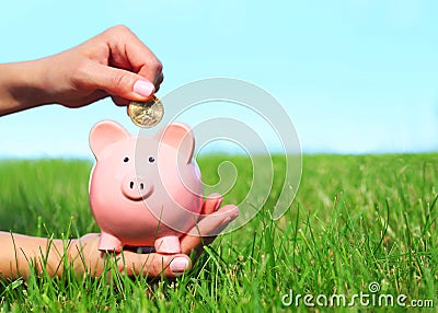 Piggy Bank and Coin in Female Hands over Green Grass Stock Photo