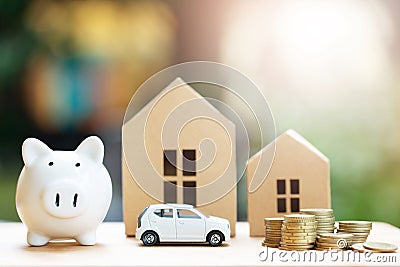 Piggy bank, Little toy car, money coins stacked on each other in different positions, house in paper model on the wooden table. Cr Stock Photo
