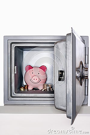 Piggy bank and piles of coins in open safe Stock Photo