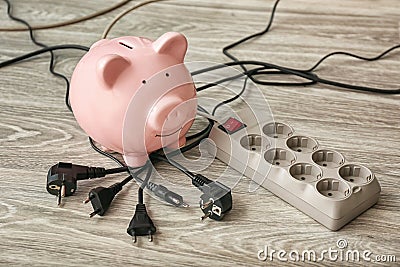 Piggy bank, plugs and power strip on floor. Electricity saving concept Stock Photo