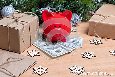 A piggy bank standing on cash dollars on a table with gift boxes, snowflakes and Christmas fir branches. Stock Photo