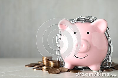 Piggy bank with steel chain and coins on table, space for text. Money safety concept Stock Photo