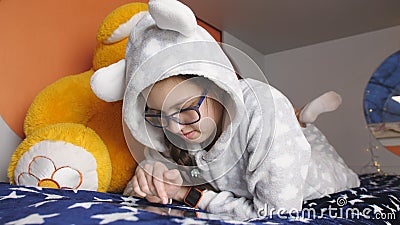 Pijamas mornos do adolescente da menina que encontram-se na cama e que jogam na tabuleta esperta video estoque Pijamas mornos do adolescente da menina que encontram-se na cama e que jogam na tabuleta esperta video estoque