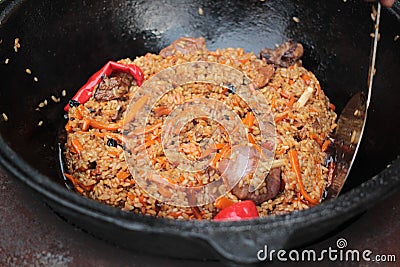 Pilaf prepare in big black cast iron with chefs hand. Stock Photo