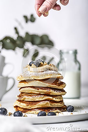 Pile of american pancakes with blueberries. Woman`s hand sifting with powdered sugar. Stock Photo