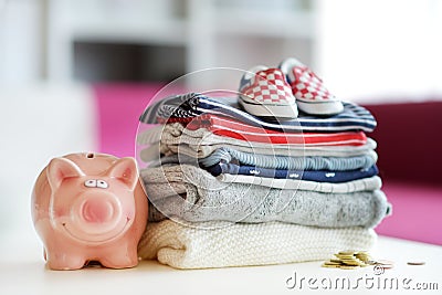 A pile of baby clothes, little shoes and a piggy bank. Parenting expenses concept. Working out a baby budget. Saving money when Stock Photo