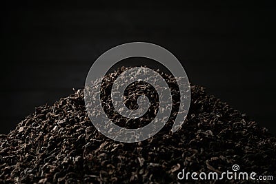 A pile of black fanning or broken loose leaf tea on a dark black background. Close-up, side view. Stock Photo