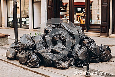 Pile of black garbage on the footpath at side road in big city, pollution trash. Many garbage plastic bags black waste Stock Photo