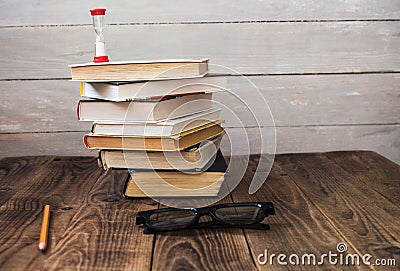 Pile of books and hourglass glasses and pencil Stock Photo