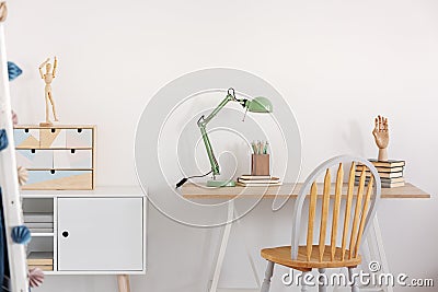 Pile of books, wooden hand and industrial mint colored lamp on stylish wooden desk in white kid`s bedroom Stock Photo