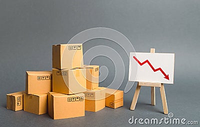 A pile of cardboard boxes and easel with red arrow down. Decrease in the quality, price, quantity and competitiveness of goods Stock Photo