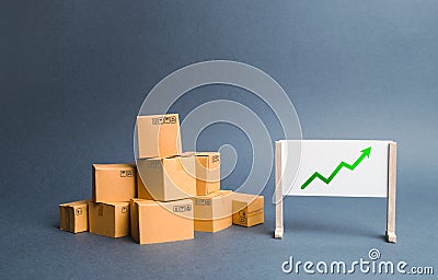 A pile of cardboard boxes and stand with green up arrow. Price increase. The growth rate of production. Increasing consumer demand Stock Photo