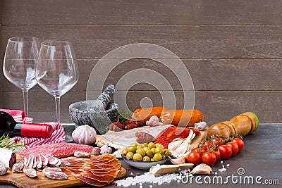 A pile of different Spanish embutido, like fuet, jamon, chorizo and lomo embuchado with red wine and two wine glasses. Stock Photo
