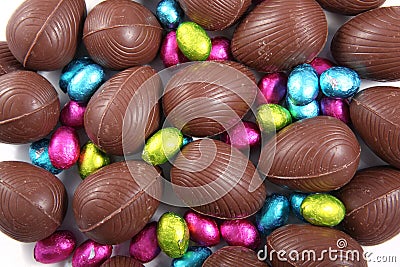 Pile of foil wrapped & unwrapped chocolate easter eggs in pink, blue & lime green, against a white background Stock Photo