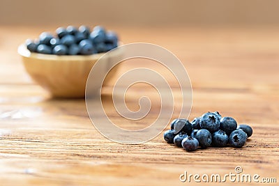 Pile of fresh blueberries with full wooden bowl on desk Stock Photo