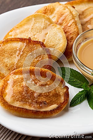 Pile of freshly fried thick pancakes, in Eastern European cuisines called oladky or oladyi with condensed milk on wooden Stock Photo