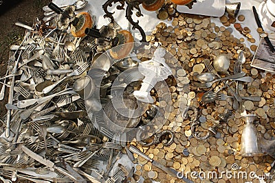 Pile of golden used coins and vintage tableware, chandelier and small statues for sale at a fair. Stock Photo