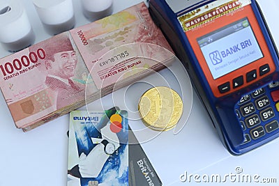 Pile of hundred thousand rupiah banknotes along with BANK BRI credit cards and bitcoins and also an EDC ELECTRONIC DATA CAPTURE Editorial Stock Photo