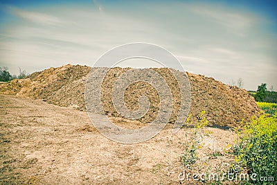 Pile of manure in the countryside with blue cloudy sky. Heap of dung in field on the farm yard with village in background Stock Photo