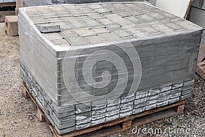 Pile of new grey paving stones on wooden pallet fixed with stretch wrap. Building material for the pavement reconstruction. Stock Photo