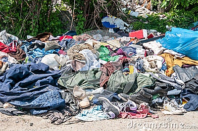 Pile of old clothes and shoes dumped on the grass as junk and garbage, littering and polluting the environment Stock Photo