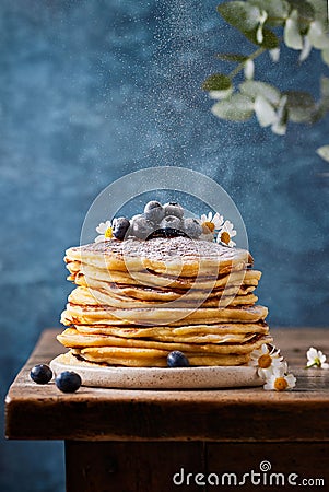Pile of pancakes topped with edible flowers and blueberries dusted with sugar powder Stock Photo