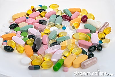 A pile of pills on a white plate symbolizing food. Vitamins on a white isolated background. Pink pills and burgundy Stock Photo