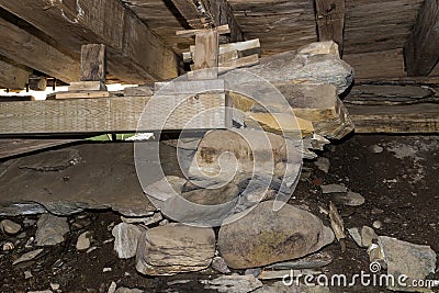 A pile of rocks, blocks of wood, and a wooden beam hold up a floor in an unfinished basement. Stock Photo