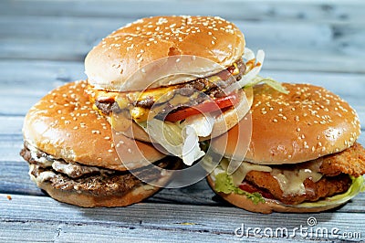 Pile of sesame buns of fried breaded chicken fillet patties, crisp lettuce, melting cheese, onions and sauce, juicy thick double Stock Photo