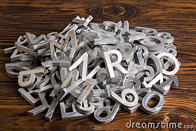Pile of silver metal alphabet characters cutted by waterjet machine in wooden background Stock Photo