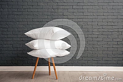 Pile of soft bed pillows on chair near brick wall Stock Photo