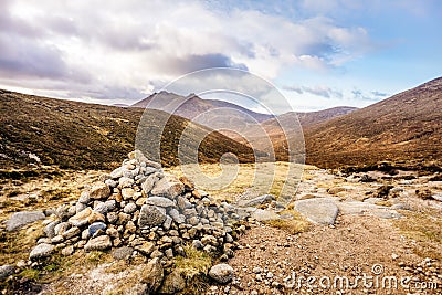 Pile of stones and footpath leading to beautiful valley in autumn colours with Mourn Mountains in background Stock Photo