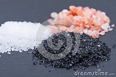 Piles of Hawaiian Black Lava Sea Salt, Coarse White Sea Salt and Himalayan Pink Salt on dark Stock Photo