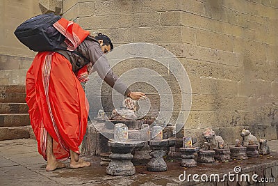 A pilgrim dressed in red doing its prayers at lingams on the river Ganges in Varanasi, India Editorial Stock Photo