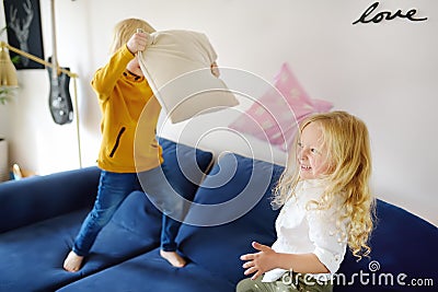 Pillow fight. Mischievous preschooler children jumping on a sofa and hitting each other with pillows. Boy and girl play together Stock Photo