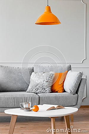 Pillows on a couch, orange lamp and coffee table in a living room interior. Real photo Stock Photo