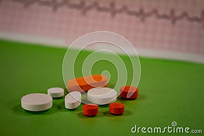 Pills of colors in a neutral background. Electrocardiogram strip out of focus Stock Photo