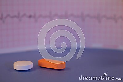 Pills of colors in a neutral background. Electrocardiogram strip out of focus Stock Photo