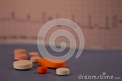 Pills of colors in a neutral background. Electrocardiogram strip out of focus Stock Photo