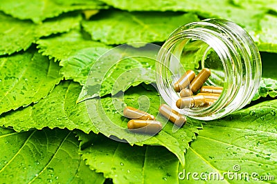 Pills in jar over green leaves. Healthy vitamin Stock Photo