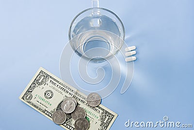 Pills organized next to a cup of water with one dollar and coins Stock Photo
