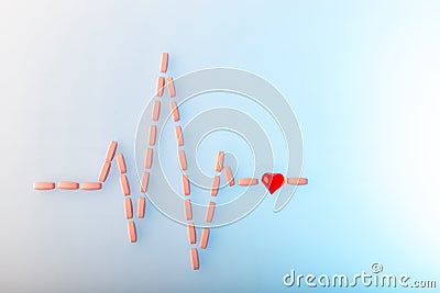 Pills in shape of cardiogram pulse on blue gradient background. Vitamins and red glass heart, symbol of healthy lifestyle. Stock Photo