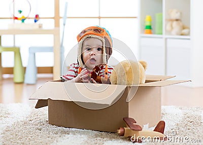 Pilot aviator baby with teddy bear toy and planes plays in cardboard box Stock Photo