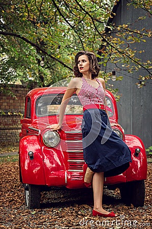 Pin-up girl posing on a red russian retro car background. A playful interested look is cast aside. Stock Photo